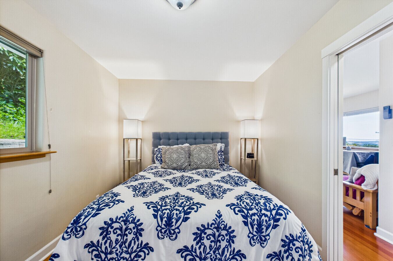 A bedroom with a large bed, two bedside lamps, a window, and a view of the outdoors.