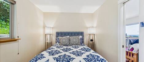 A bedroom with a large bed, two bedside lamps, a window, and a view of the outdoors.