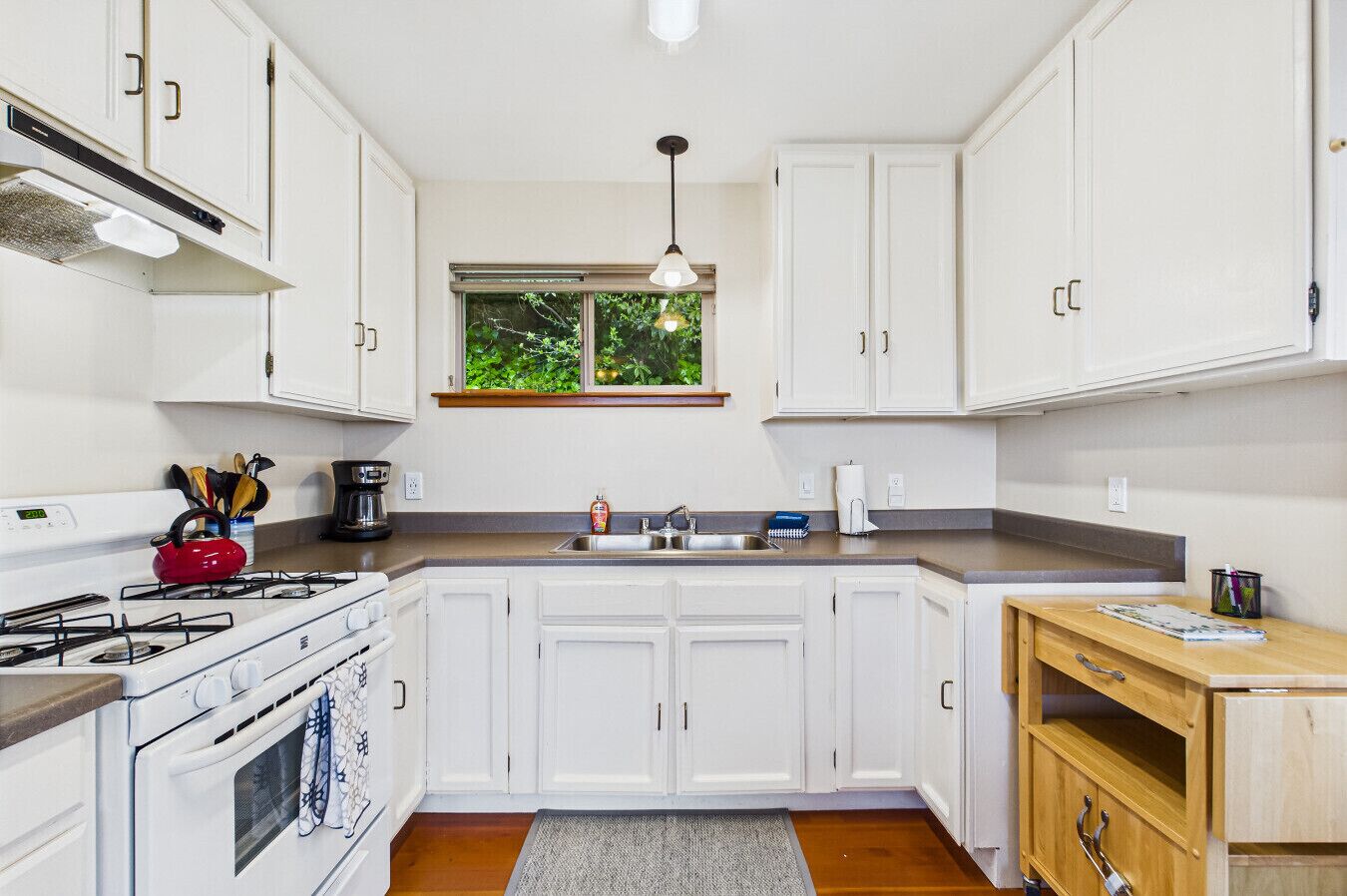 A modern kitchen with white cabinets, a stove, a sink, and a window with a view of greenery.
