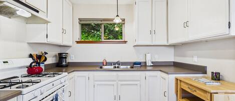 A modern kitchen with white cabinets, a stove, a sink, and a window with a view of greenery.
