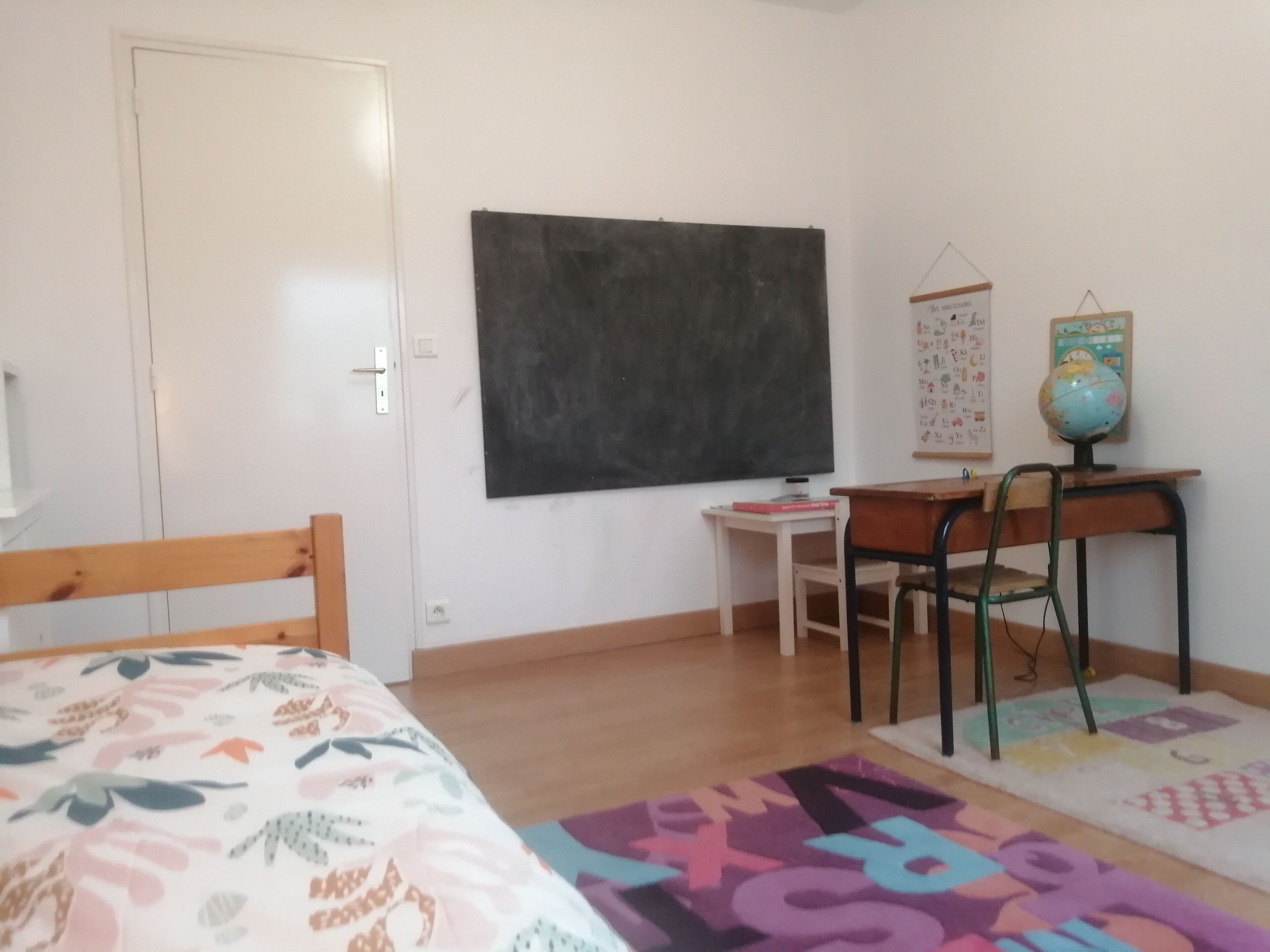 Un dormitorio con una cama, un escritorio, una silla, una pizarra y un globo terráqueo.