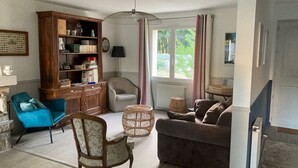 A living room with a wooden cabinet, a blue chair, a brown sofa, and a wicker side table. - Large family home in Mesquer (Mesquer)