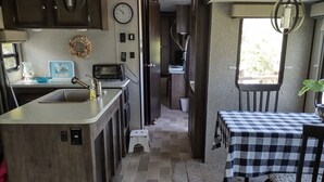 A compact kitchen with a central island, a dining area with a checkered tablecloth, and a cozy seating area. -  Port Saint Joe 1/1 Trailer that sleeps 4, only 2 blocks to Beach -Pet friendly! (Port St. Joe)