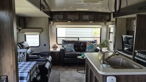 A compact RV interior with a kitchenette, a seating area with a sofa and a table, and a small window providing natural light. -  Port Saint Joe 1/1 Trailer that sleeps 4, only 2 blocks to Beach -Pet friendly! (Port St. Joe)