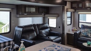 A compact RV interior with a kitchenette, a black leather sofa, a small dining table, and a ceiling fan. -  Port Saint Joe 1/1 Trailer that sleeps 4, only 2 blocks to Beach -Pet friendly! (Port St. Joe)