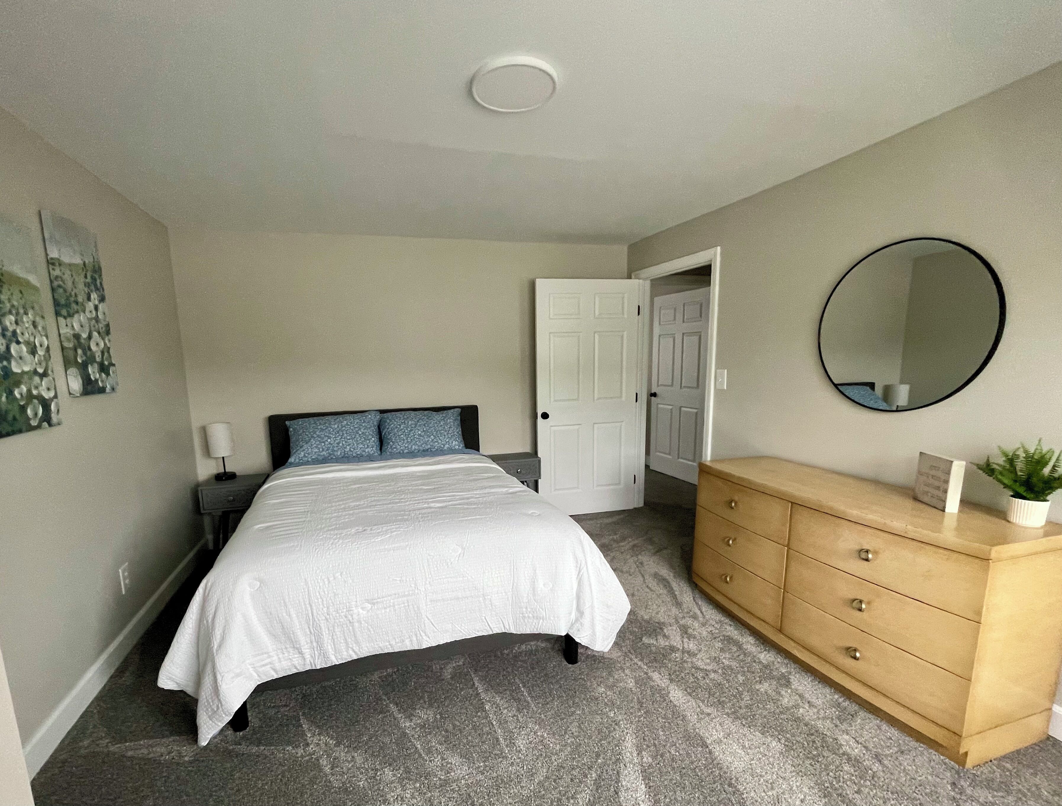 Une chambre à coucher avec un lit, une commode, un miroir et une porte.