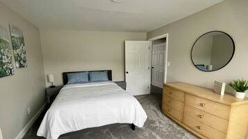 Une chambre à coucher avec un lit, une commode, un miroir et une porte.