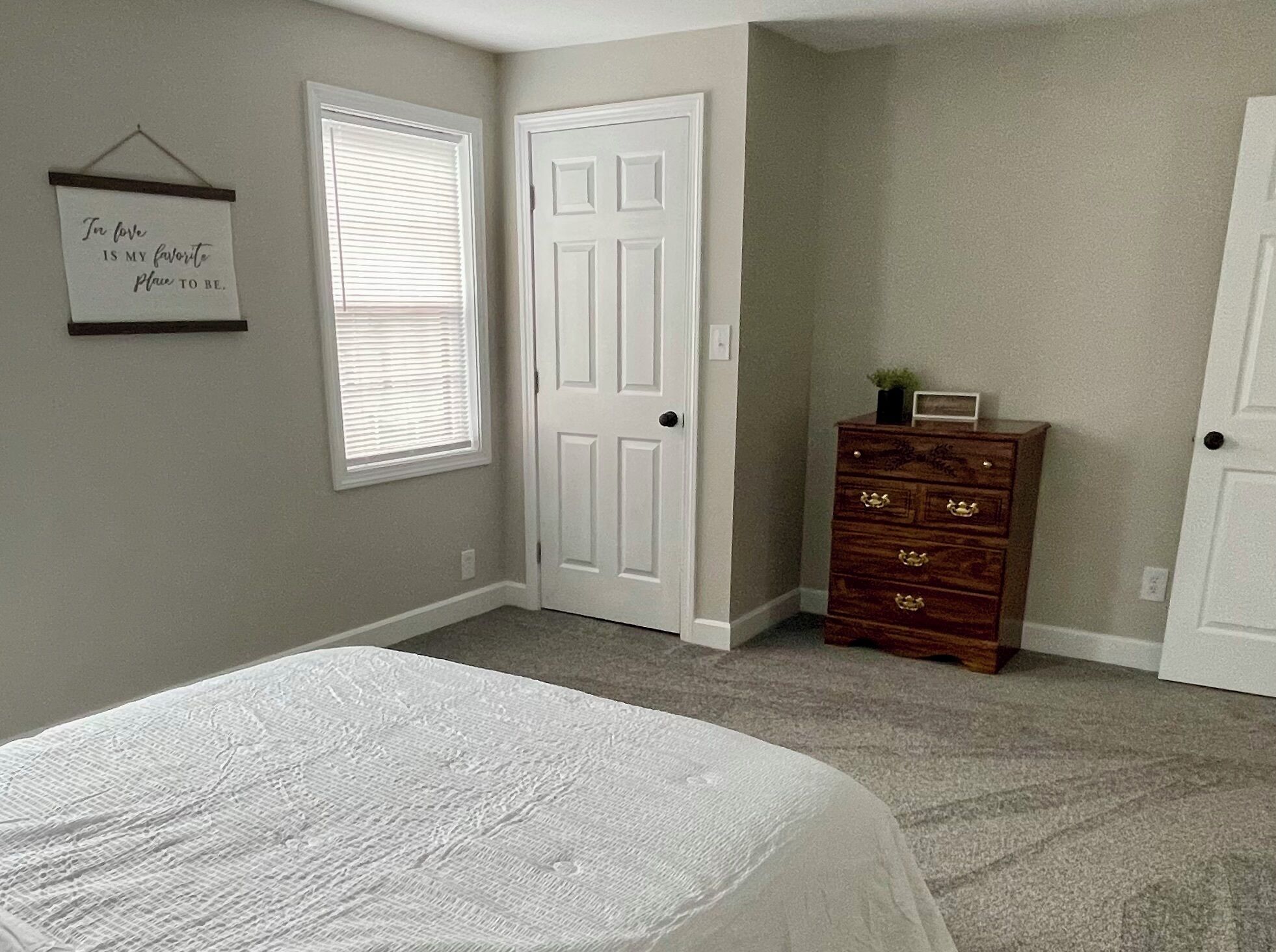 Une chambre à coucher avec un lit, deux portes, une commode et un panneau fixé au mur.