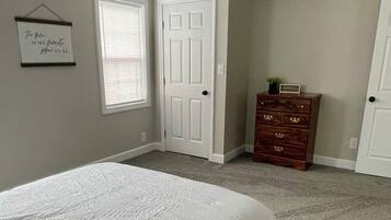 Un dormitorio con cama, dos puertas, cómoda y cartel en la pared.