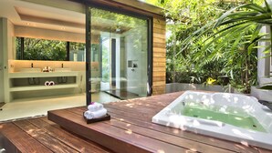 Un baño moderno con cabina de ducha de vidrio, un banco de madera con toallas y un jacuzzi.