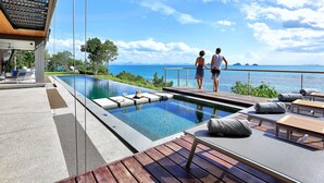 Zona de piscina con vista al mar, sillas de descanso y una terraza de madera.