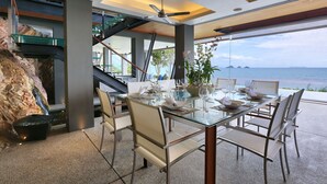 Un comedor con una mesa de vidrio y sillas, una planta en maceta y vista al mar.