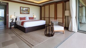 A spacious bedroom with a large bed, a sitting area with a chair, and a view through a glass door.