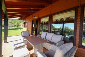 A covered patio with wicker furniture, large windows, and a view of the outdoors.