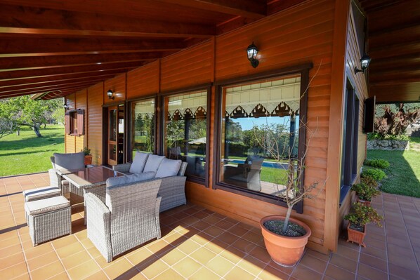 A covered patio with wicker furniture, large windows, and potted plants.