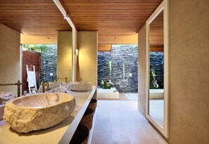 Une salle de bain moderne avec un grand lavabo en pierre, un plafond en bois et une vue sur un mur de pierre et des plantes.
