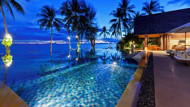 A swimming pool with a tiled floor, surrounded by palm trees and a view of the ocean.