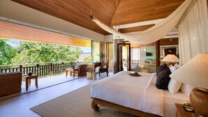 A spacious bedroom with a large bed, a wooden desk, and a balcony with a view of lush greenery.