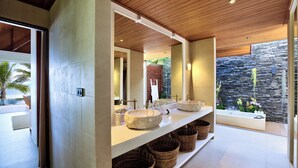 A modern bathroom with a stone sink, a large mirror, and wicker baskets on the counter.
