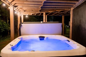 Un bain à remous sous une pergola en bois, avec vue sur le jardin environnant.