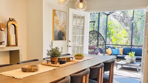 A dining area with a long wooden table, black upholstered chairs, and hanging pendant lights.