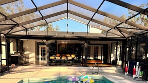 A covered outdoor pool area with a barbecue setup and a dining table.