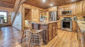 Un interno rustico con pavimenti in legno, un'isola centrale con sgabelli, una cucina con elettrodomestici in acciaio inossidabile e una scala che conduce a un piano superiore.