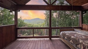 Una baita di legno con un letto e un balcone con vista su una catena montuosa boscosa.