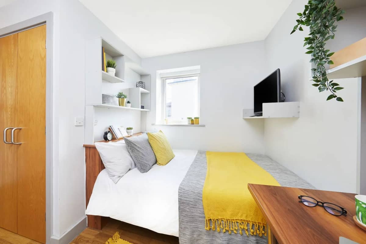 Une chambre à coucher de taille réduite, comprenant un lit, une table de chevet et un téléviseur fixé au mur.