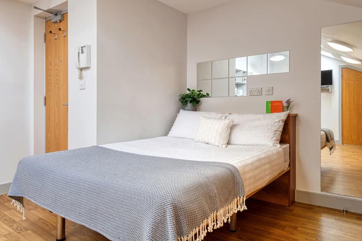 Une chambre à coucher moderne avec un lit, une porte en bois, un téléphone, un miroir et une plante.