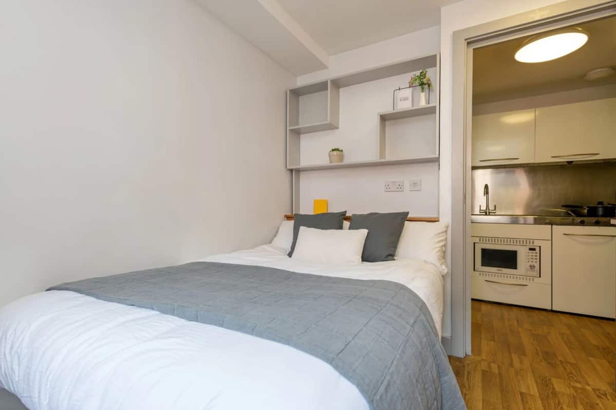 Une chambre moderne avec un lit, une petite kitchenette et un plancher en bois.