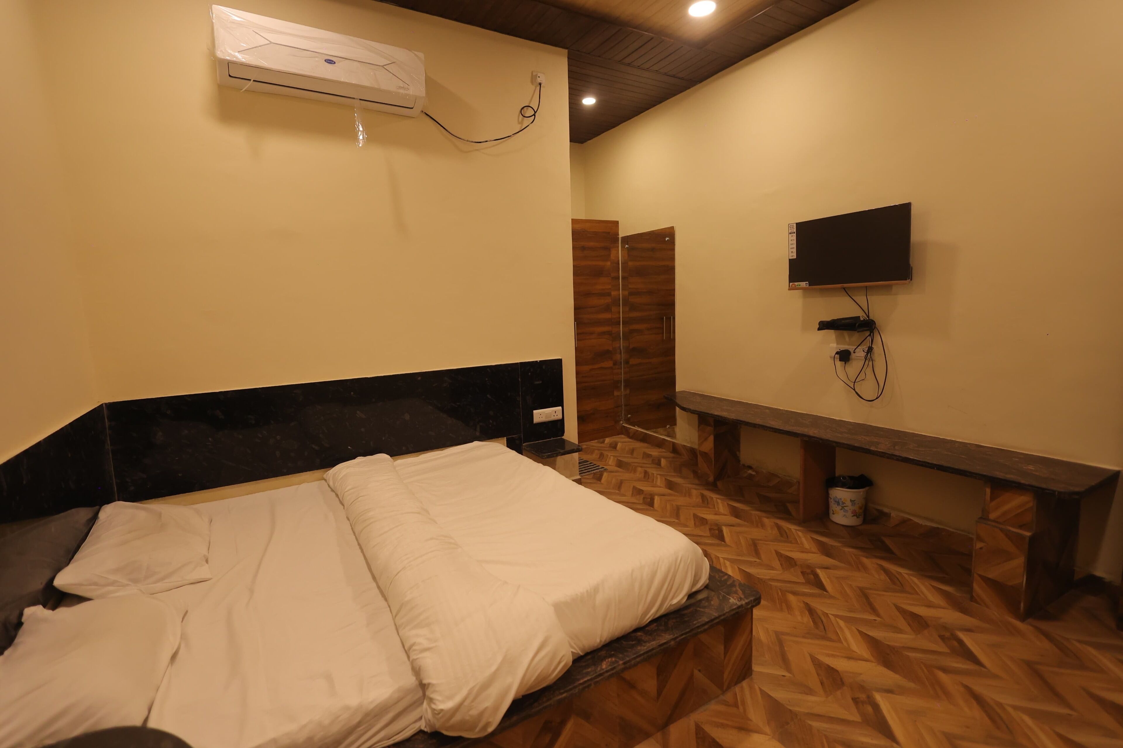 A hotel room with a bed, a TV mounted on the wall, and a wooden bench.