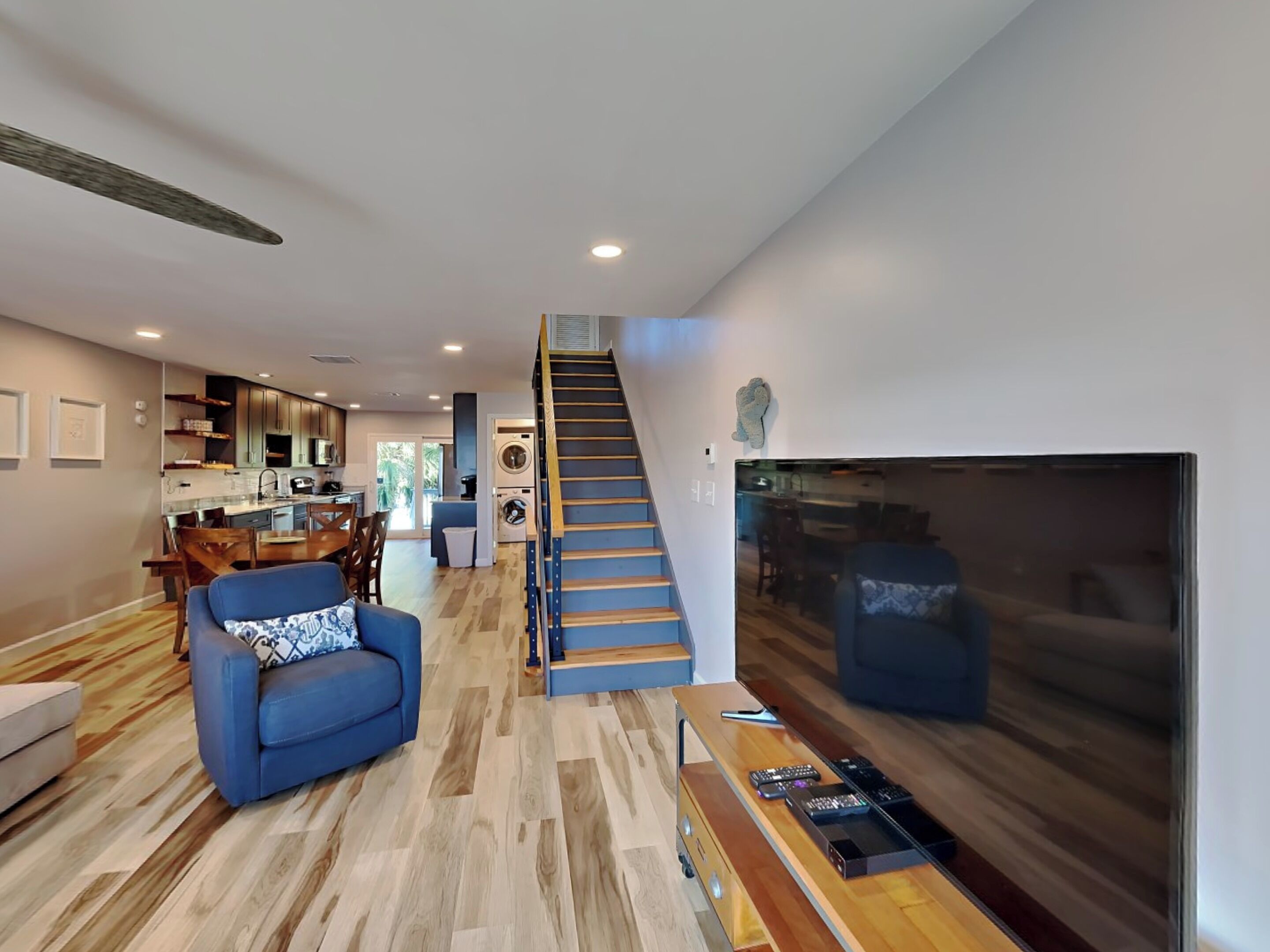 A modern living room with a blue sofa, wooden flooring, a staircase, and a large TV.