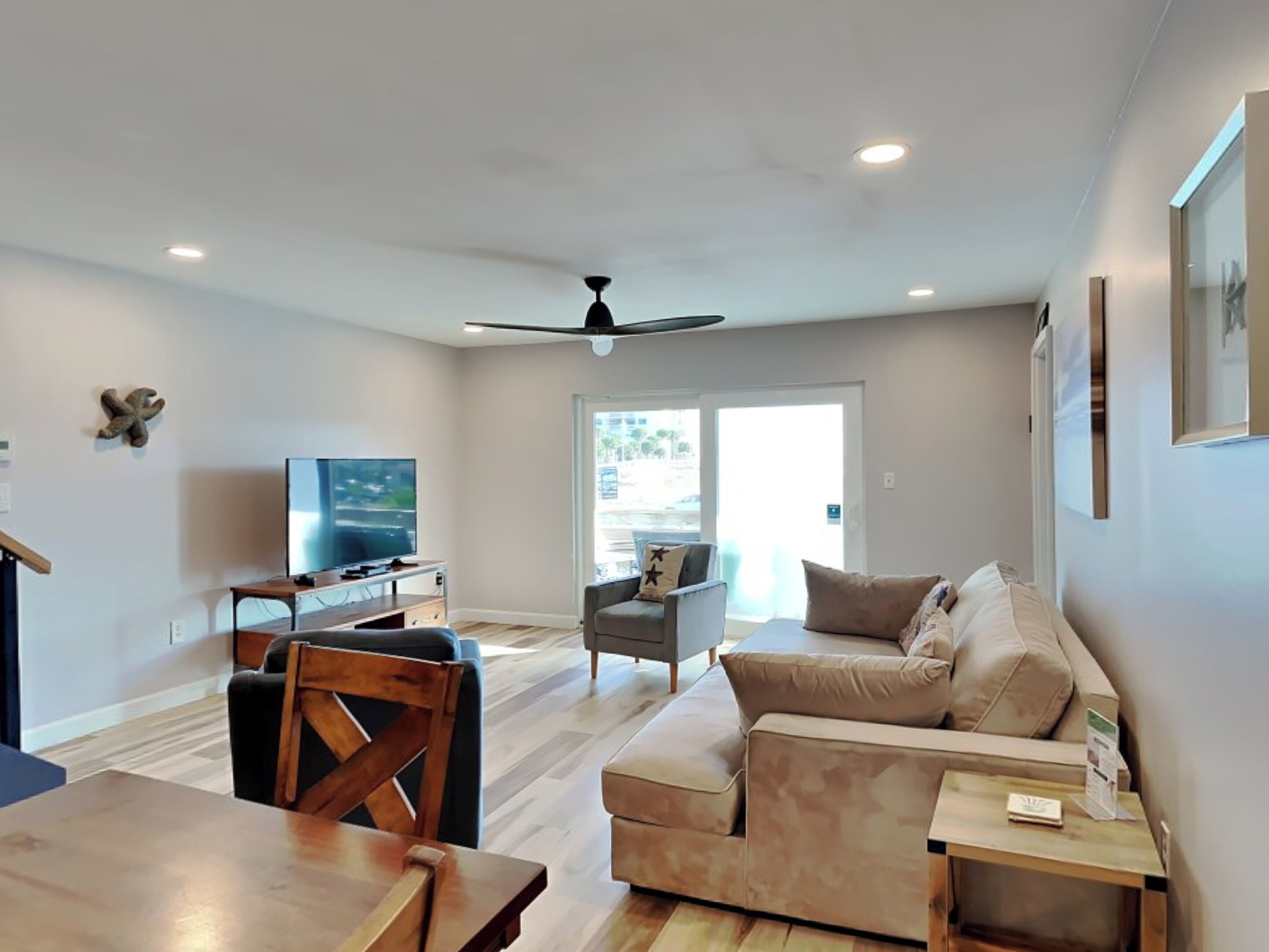 A modern living room with a flat-screen TV, a ceiling fan, and a dining area with a wooden table and chairs.