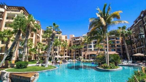 Een resort met meerdere zwembaden, palmbomen en een helderblauwe lucht.