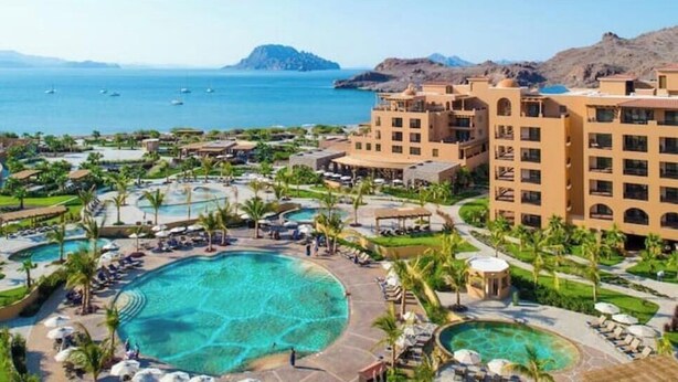 Un resort con varias piscinas, un edificio grande y vista al mar.