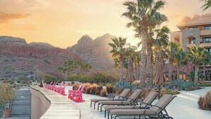 Zona de piscina en un resort, con sillas reclinables y palmeras, con vistas a un paisaje montañoso.