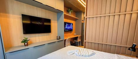 Une chambre d’hôtel avec un lit, un téléviseur fixé au mur, un bureau avec une chaise et une plante.