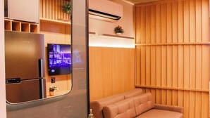 A modern hotel room with a built-in refrigerator, a flat-screen TV, a sofa, and a wooden panel wall. - Setai Yacht Premium II - By Almare Flats (João Pessoa)