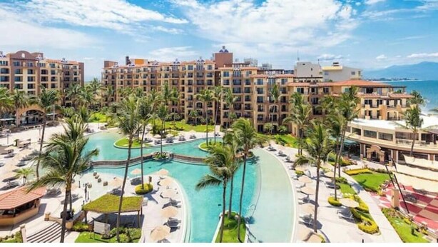 Ein Resort mit mehreren Gebäuden, einem zentral gelegenen Pool und Palmen.