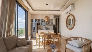 A modern living room with a sofa, a round dining table with chairs, a wicker armchair, and a small table with a vase. - Luxury Modern Beachfront Apartment - Incredible Sunrise and Sunset View (Puerto Morelos)