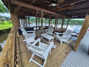 A wooden deck with white Adirondack chairs and a table, overlooking a lake.