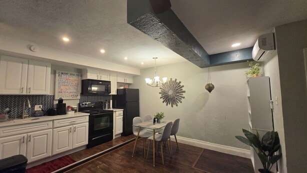 Una cocina moderna con armarios blancos, un microondas negro y una zona de comedor con mesa y sillas de vidrio.