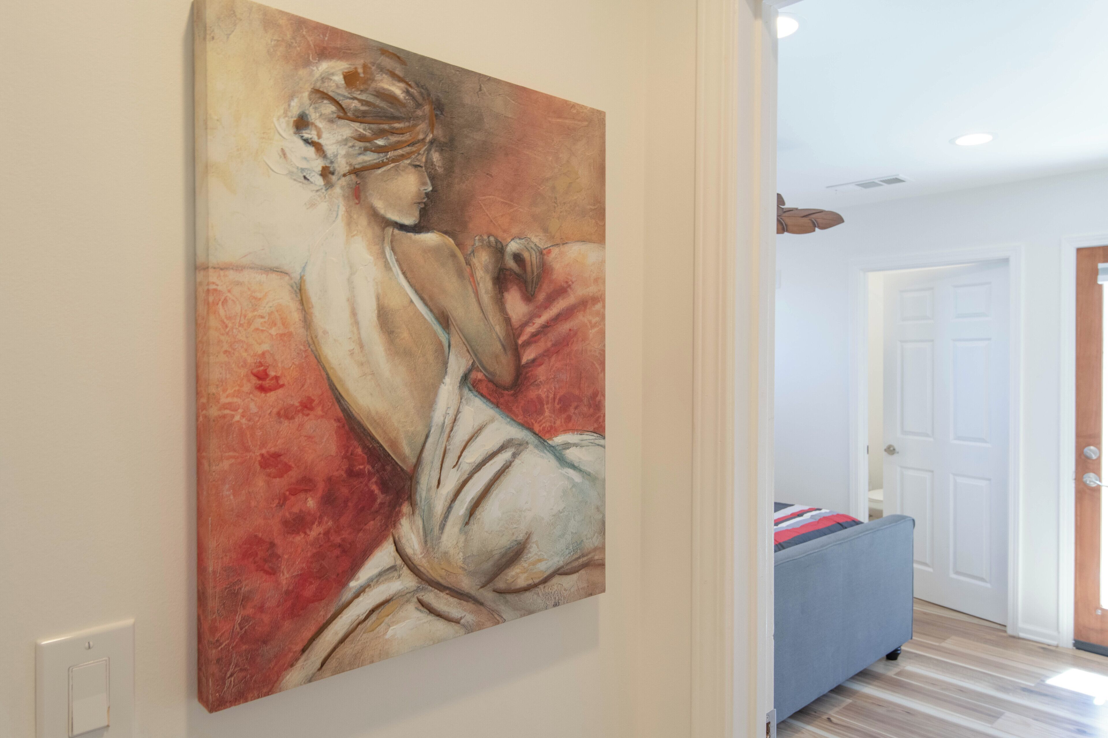 A hallway with a large painting on the wall, a door, and a blue bench.