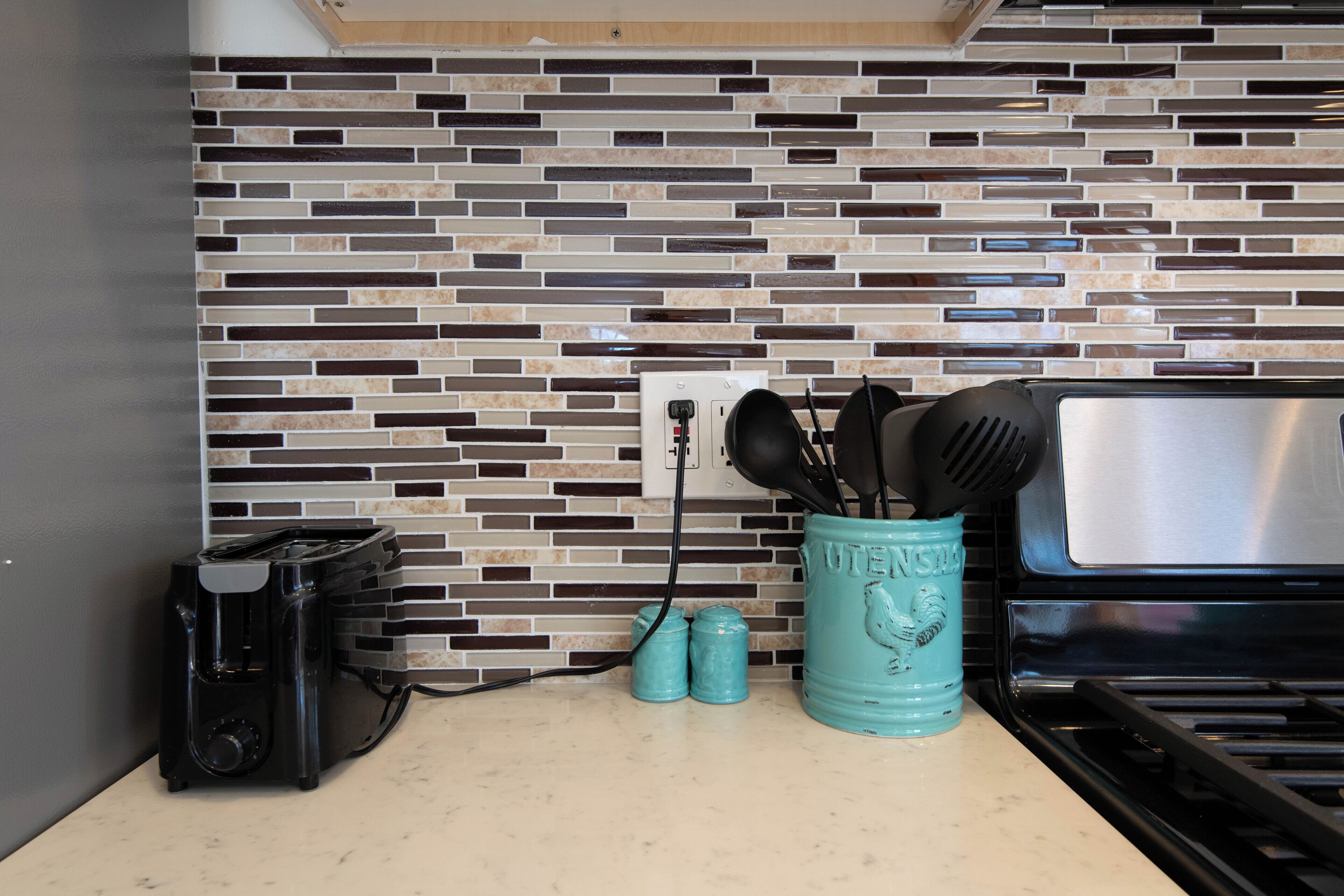 Une cuisine avec un mur recouvert de carreaux, un grille-pain, un porte-épices et une cuisinière.