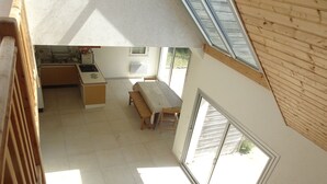 Une pièce aux hauts plafonds comprenant un coin cuisine, une table à manger avec des bancs, et une grande porte-fenêtre coulissante donnant sur un espace extérieur.