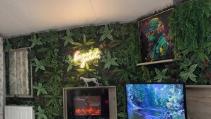 Un salon doté d’une cheminée, d’un téléviseur et d’un mur décoré de feuillages verts et d’un néon.
