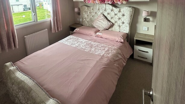 Une chambre à coucher comprenant un lit, une tête de lit ornée de motifs floraux, une table de chevet, une commode et une fenêtre avec des rideaux.
