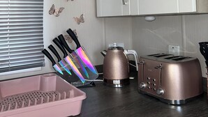 Une cuisine avec des meubles blancs, un grille-pain, une bouilloire et un récipient rose.
