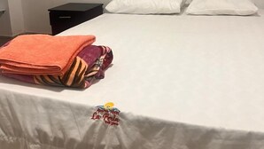 Un lit avec des draps blancs, une tête de lit noire et une serviette orange soigneusement pliée, posée sur le côté.